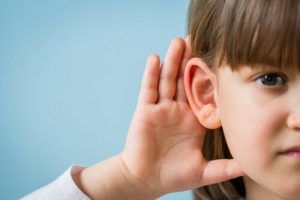 Niña que no oye bien y se pone la mano en el oído para explicar los tipos de pérdida auditiva